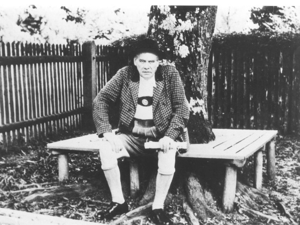 oskar-maria-graf-unter-einem-baum, um den eine Bank gebaut ist, alte Zäune im Hintergrund